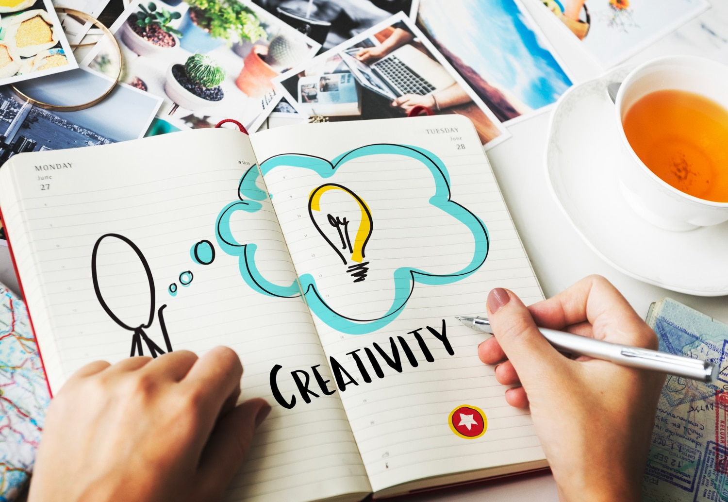 Open notebook showing a doodle of a light bulb and the word creativity, surrounded by travel and lifestyle photos with a cup of tea.
