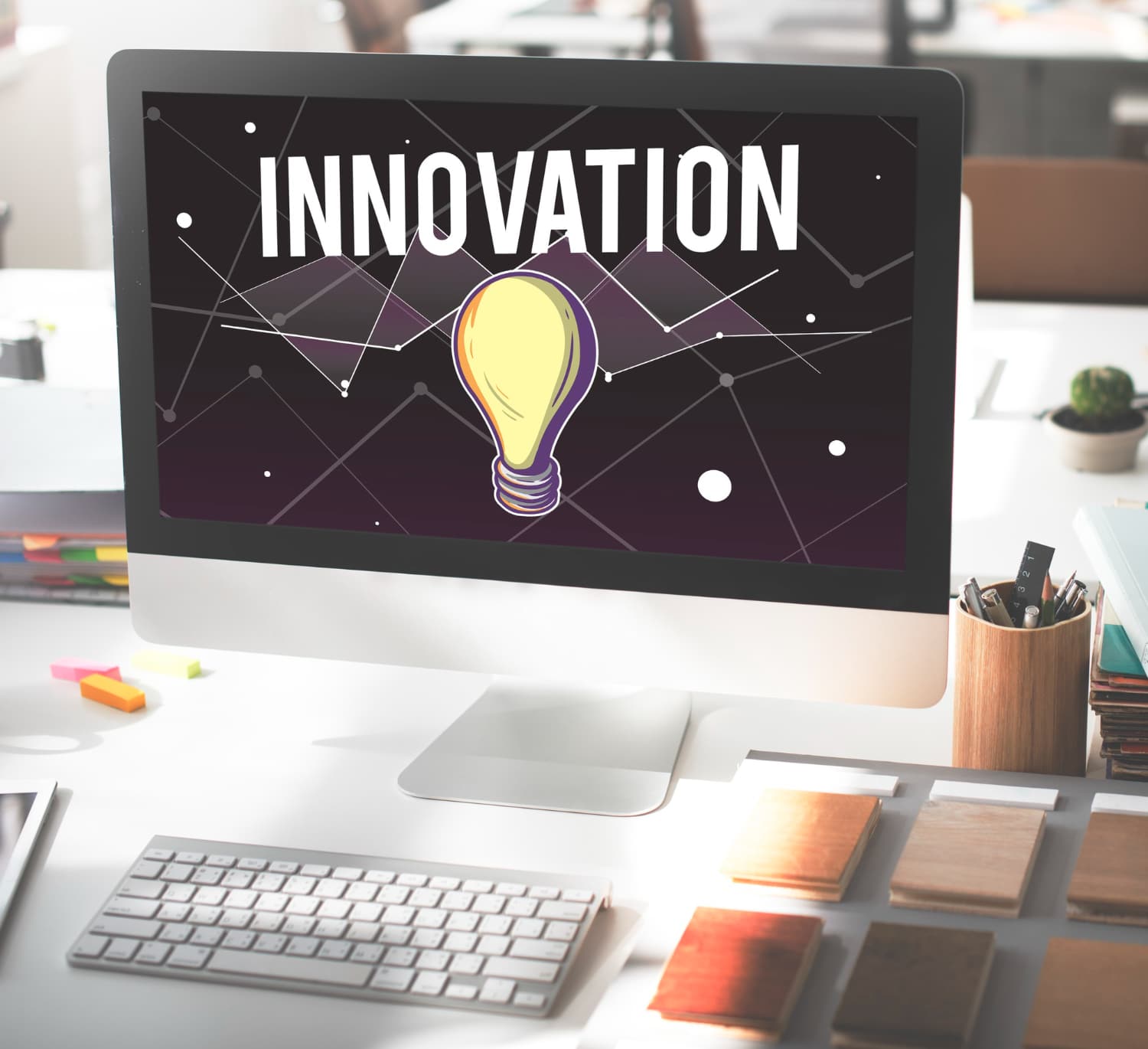 A desktop computer screen displaying the word INNOVATION with a graphic of a light bulb, set in a modern office environment.