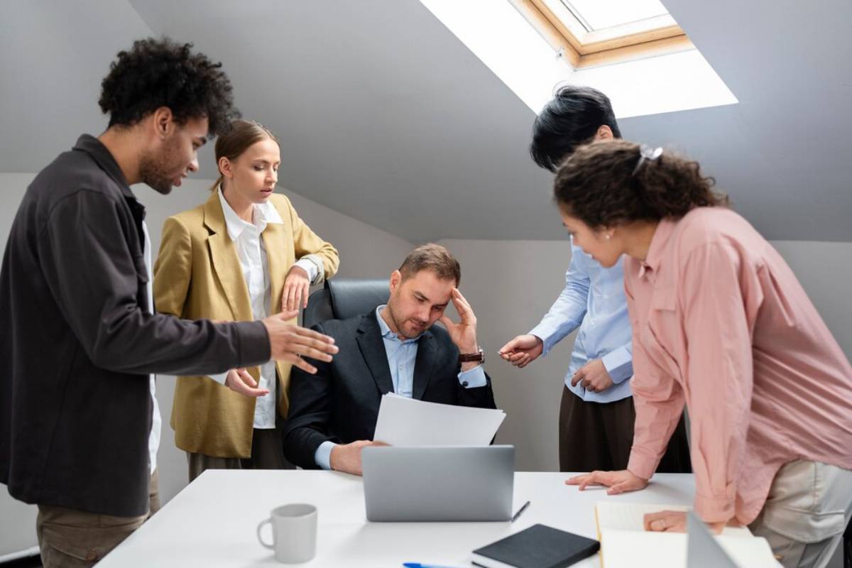 A group of colleagues discussing work around a laptop in a brightly lit office.