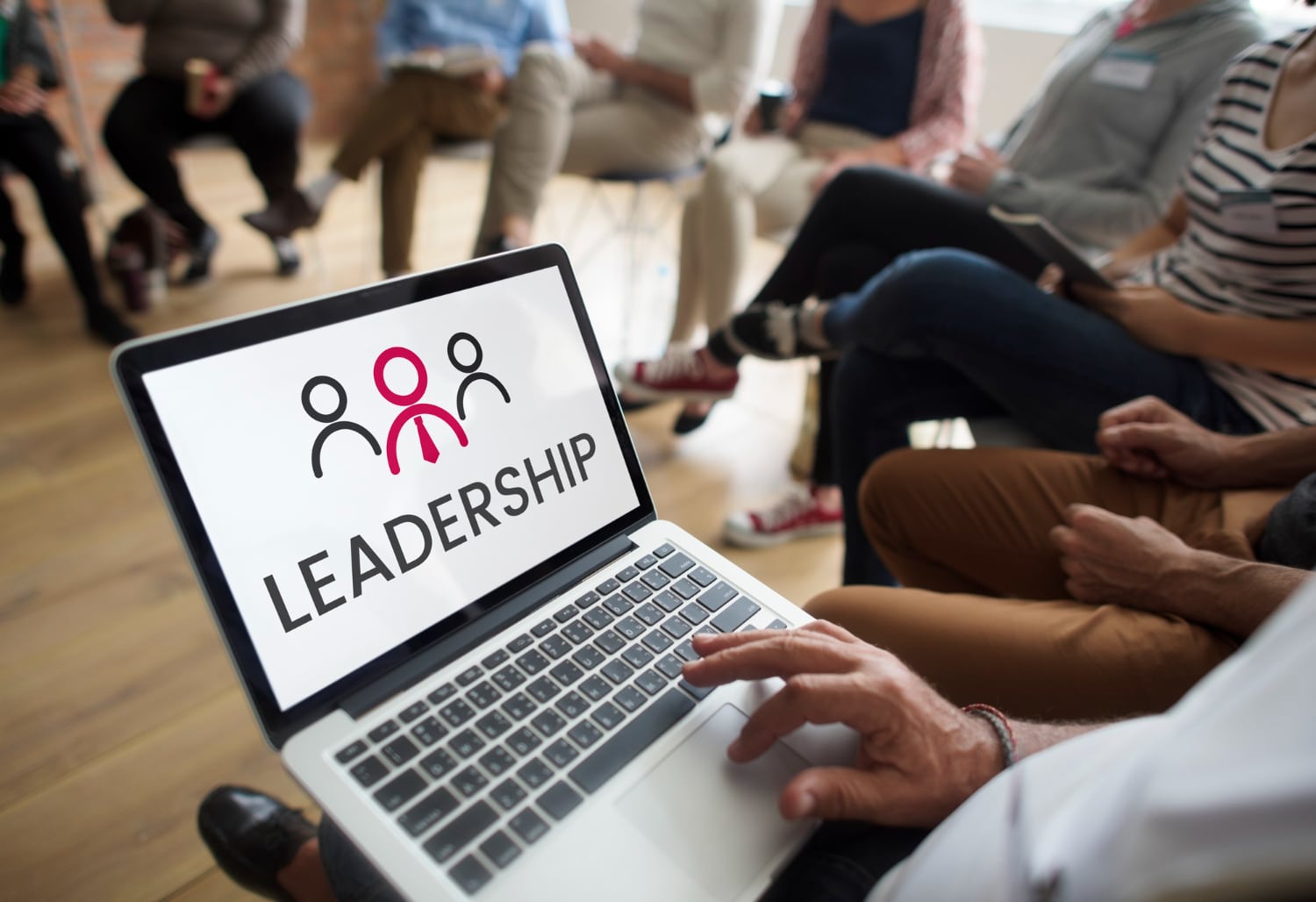 Laptop screen displaying "Leadership" at a workshop with participants seated around in blurred background.