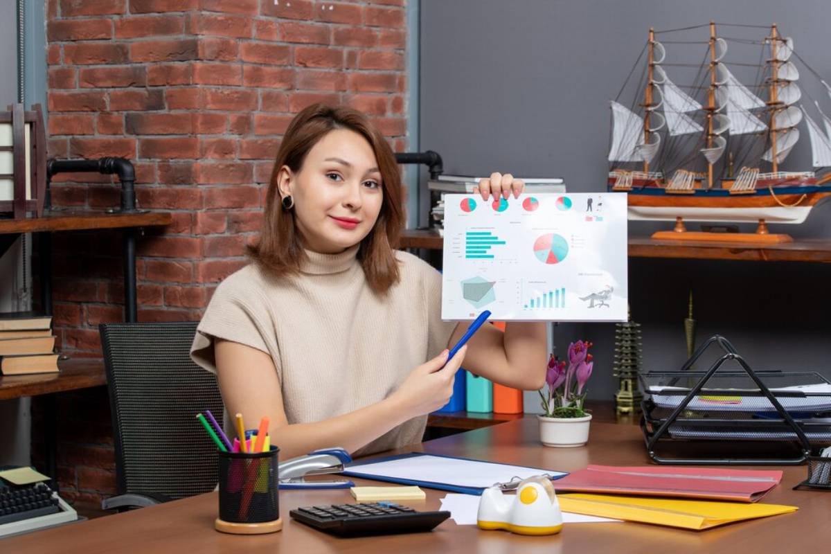 A young woman presents a statistical report in a stylish office with a brick wall backdrop.
