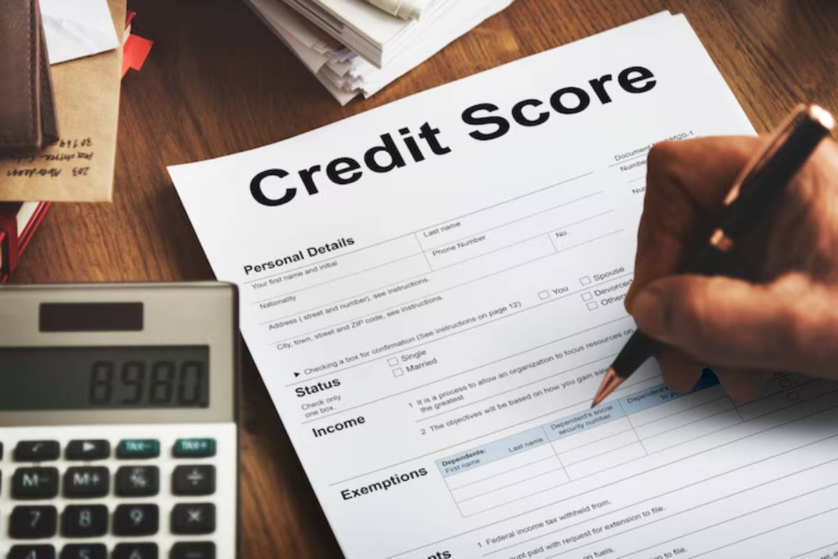 Close-up of hands filling out a credit score form with personal details, a calculator, and scattered papers in the background.